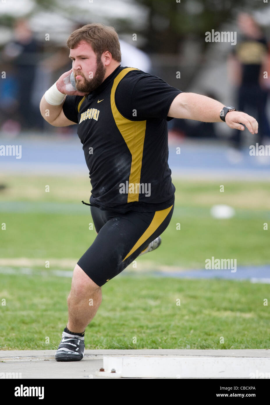 A male athlete throws a shot put during a track and field meet Stock