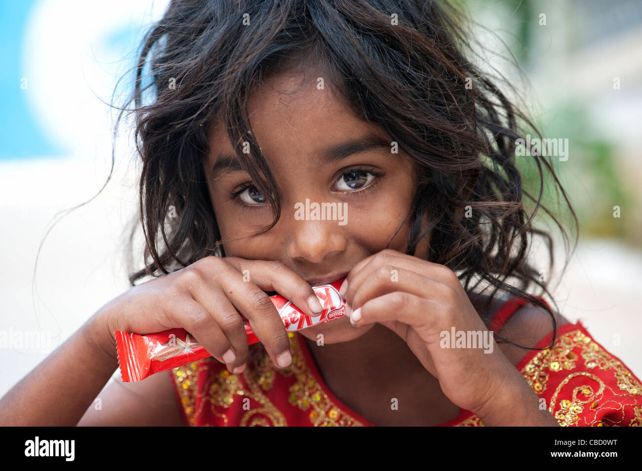 Young poor lower caste Indian street girl holding and eating a chocolate bar. Andhra Pradesh, India Stock Photo