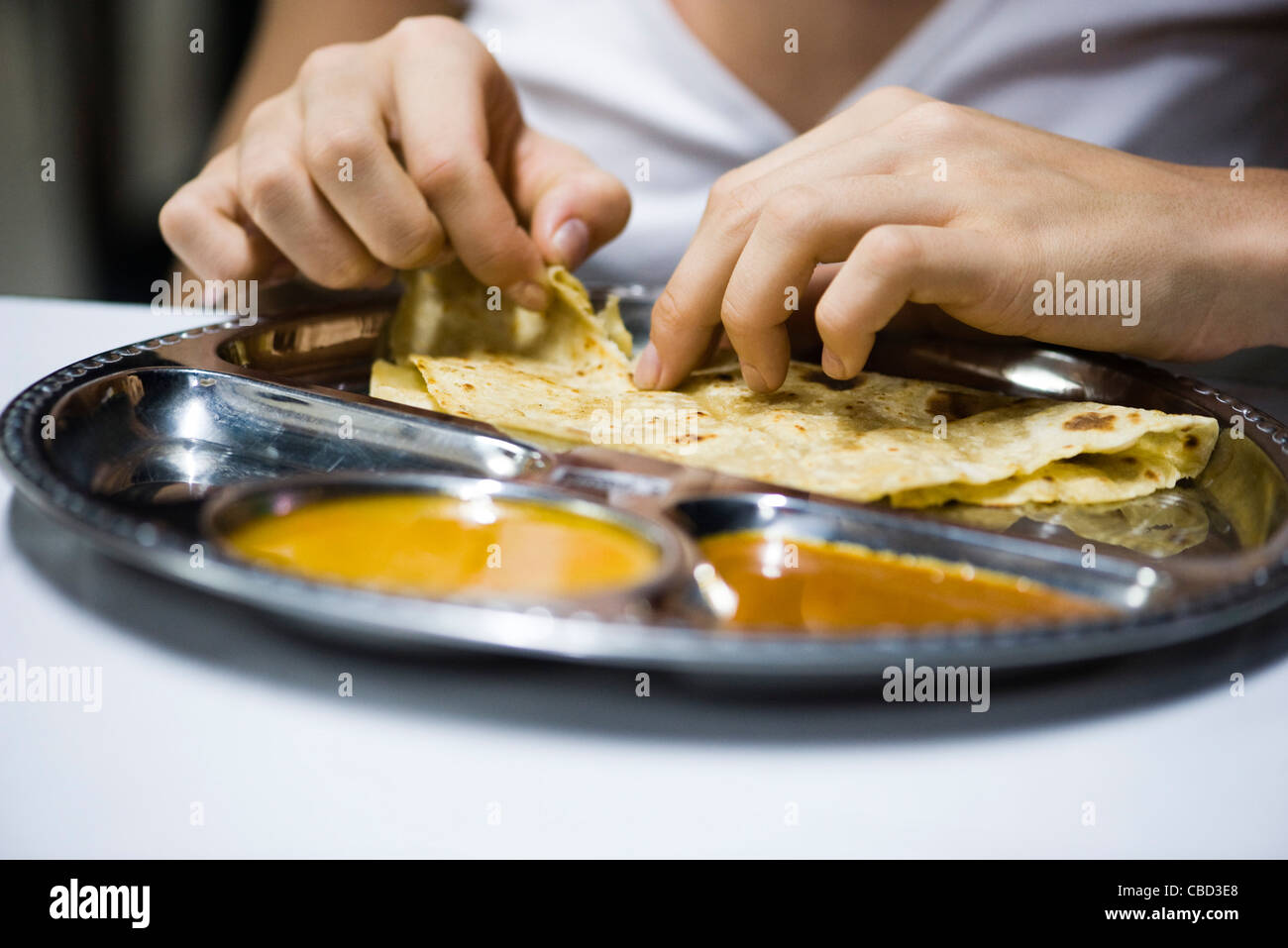 Person eating roti canai with curry, cropped Stock Photo