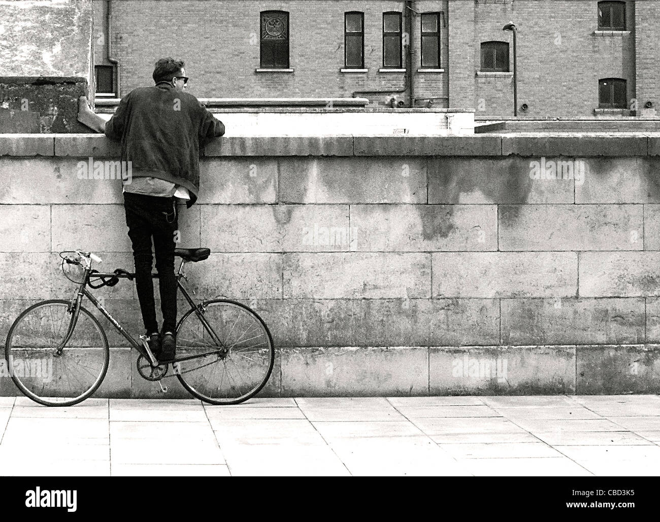 fashionable east londoner perched on fixie bike looking over wall Stock Photo