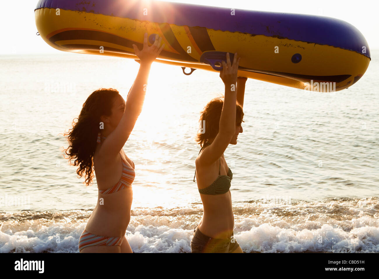 Women carrying inflatable boat on beach Stock Photo