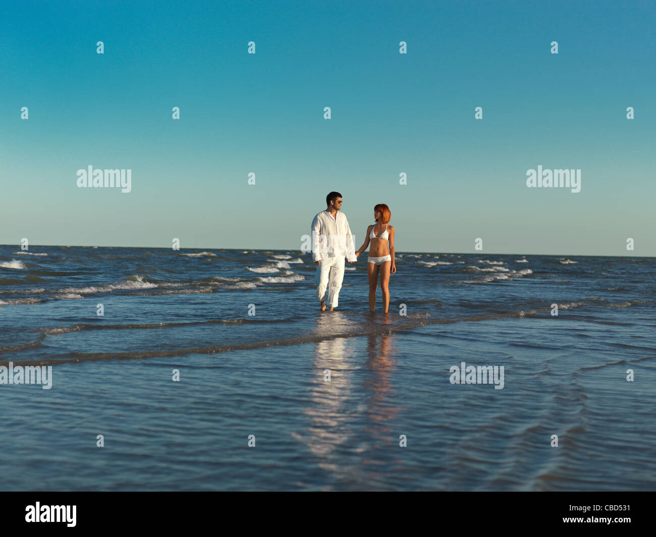 happy, young couple, dressed in white, walking in the water by the sea shore, holding hands Stock Photo