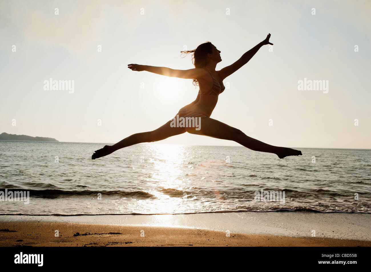 Woman leaping over waves on beach Stock Photo