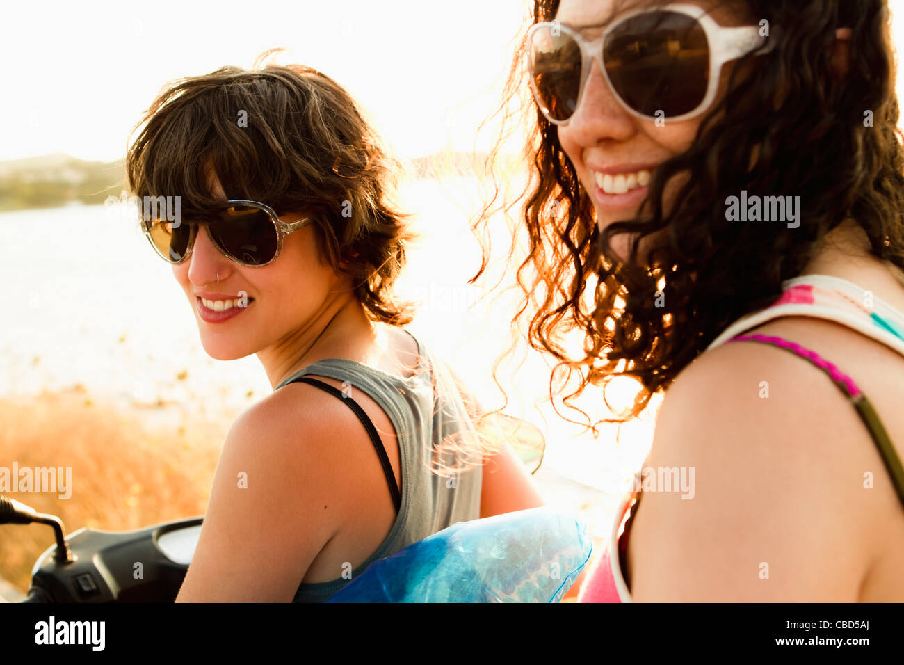 Smiling women riding scooter on beach Stock Photo