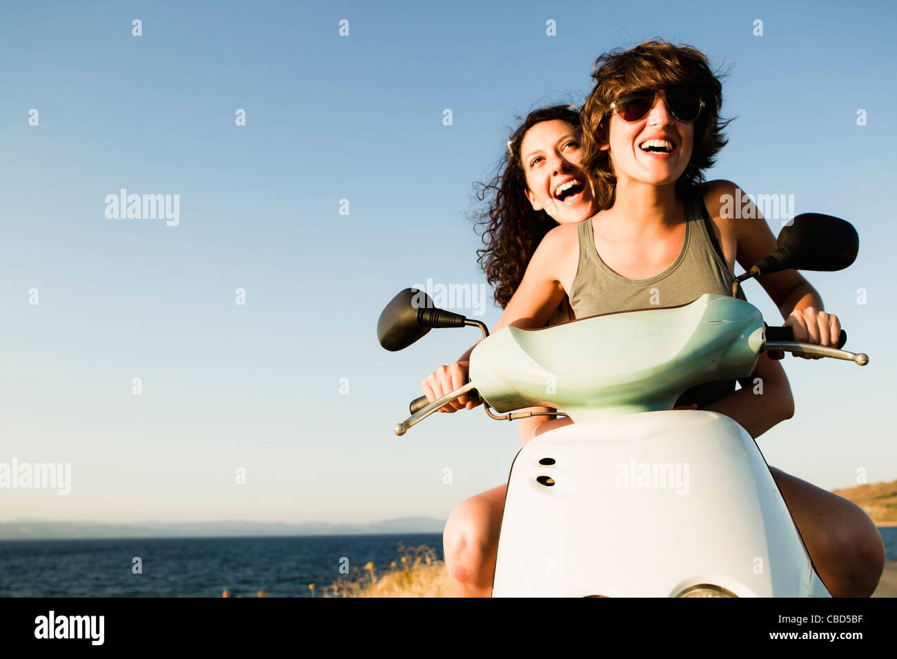 Smiling women riding scooter on beach Stock Photo