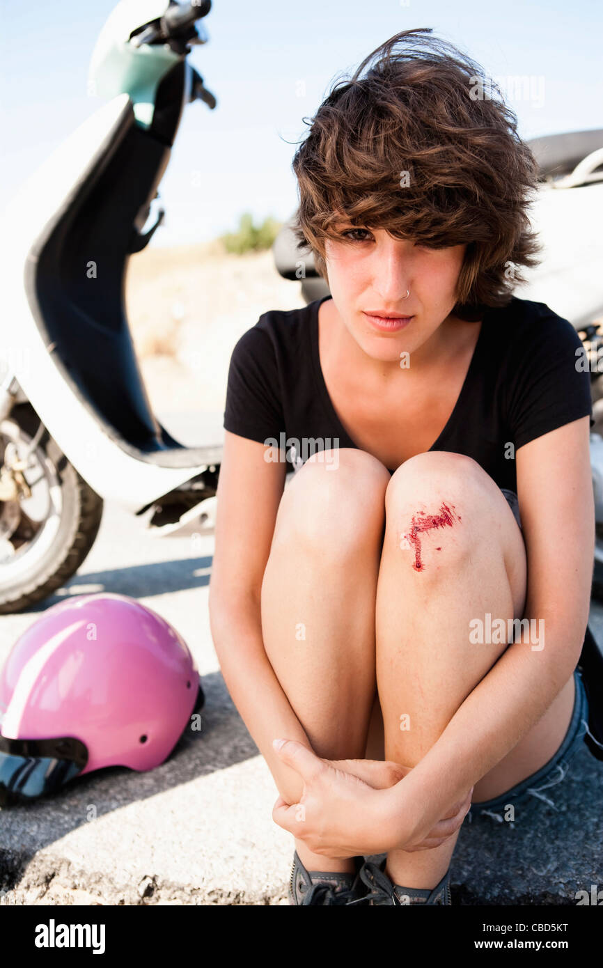Woman with scooter nursing scraped knee Stock Photo