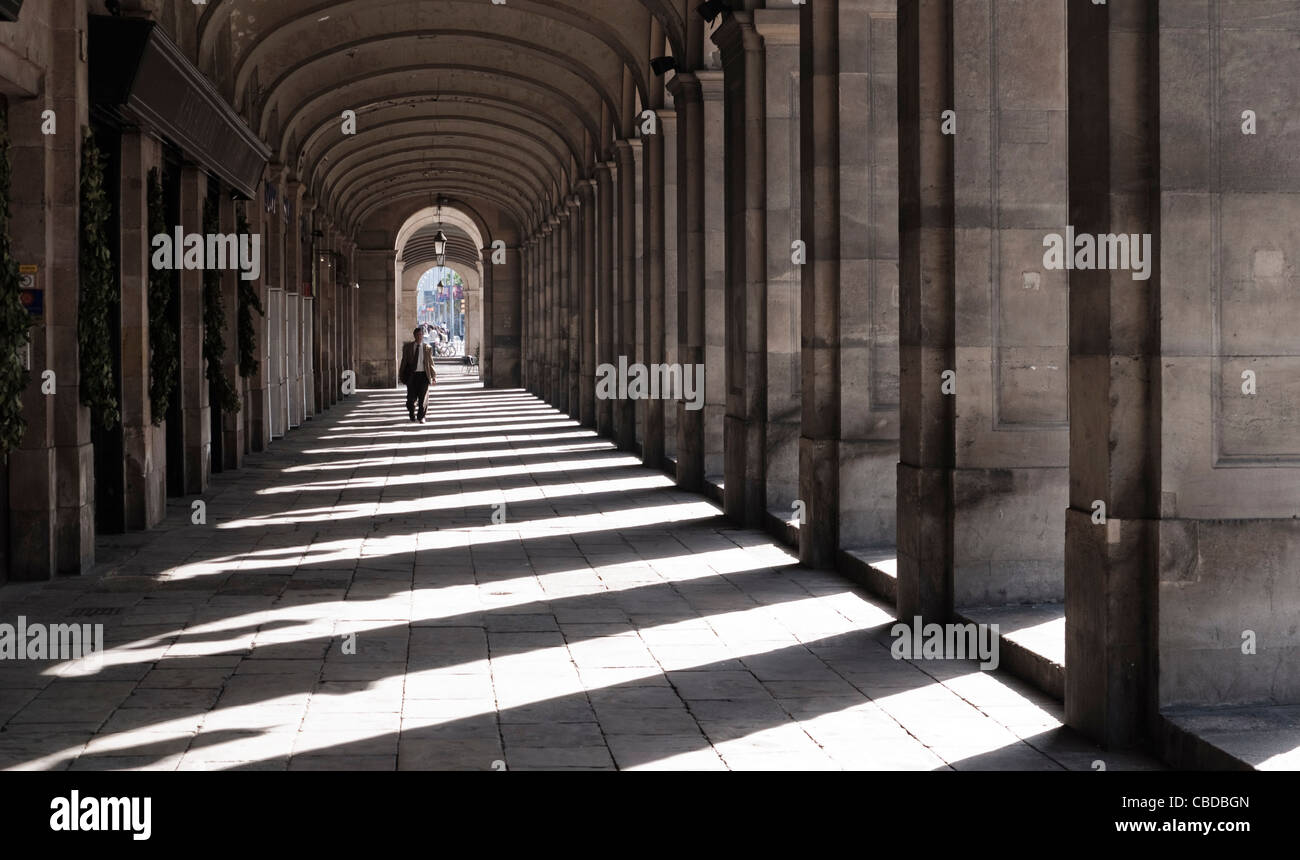 A man in silhouette walking down the Passieg D'Isabel, Barcelona with harsh shadows cast by the arches. Stock Photo