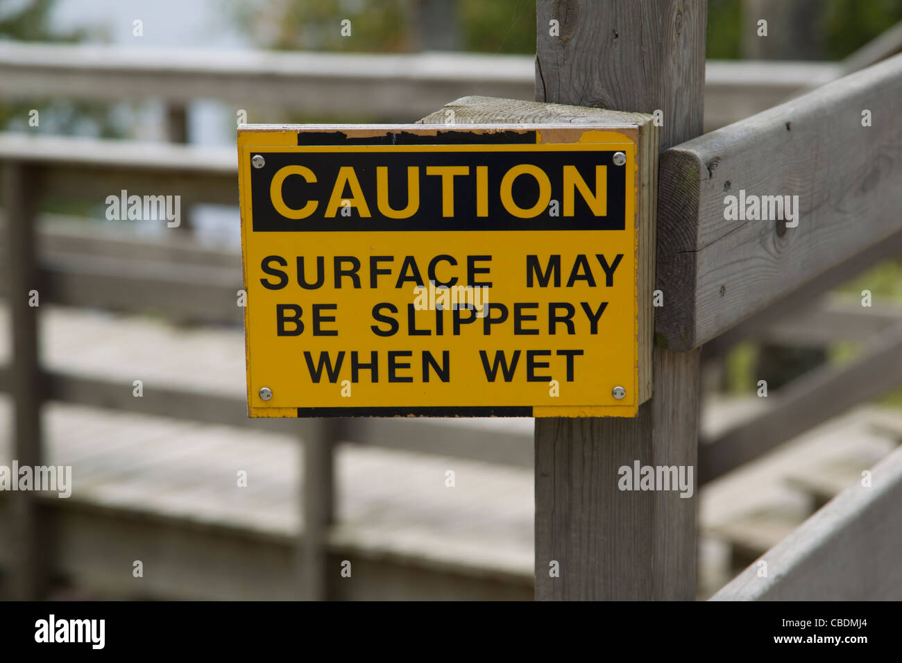 A yellow and black sign that reads Caution Surface may be Slippery when Wet. Stock Photo