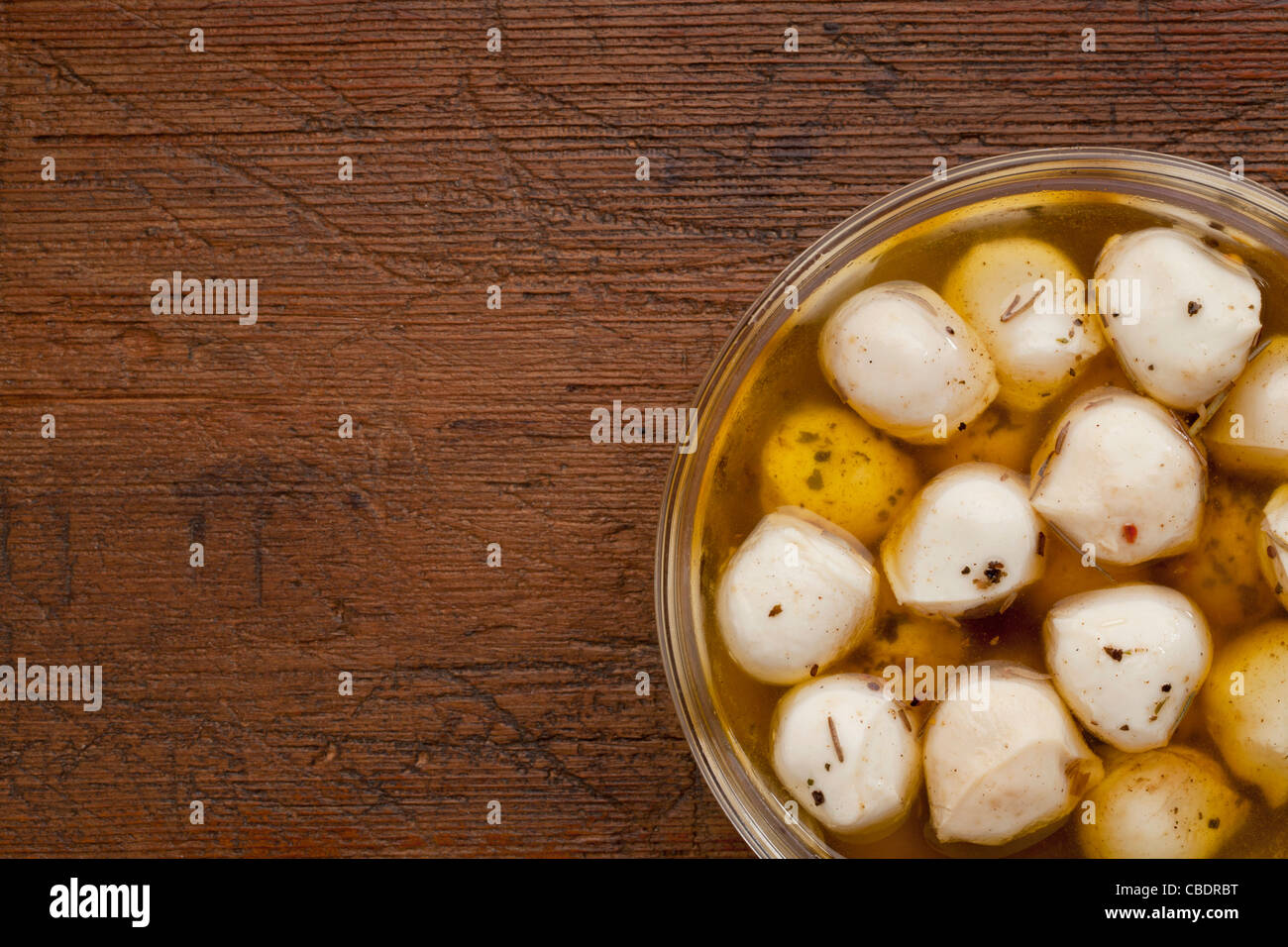 balls of mozzarella cheese marinated in oil with seasoning, glass bowl on weathered wood background Stock Photo