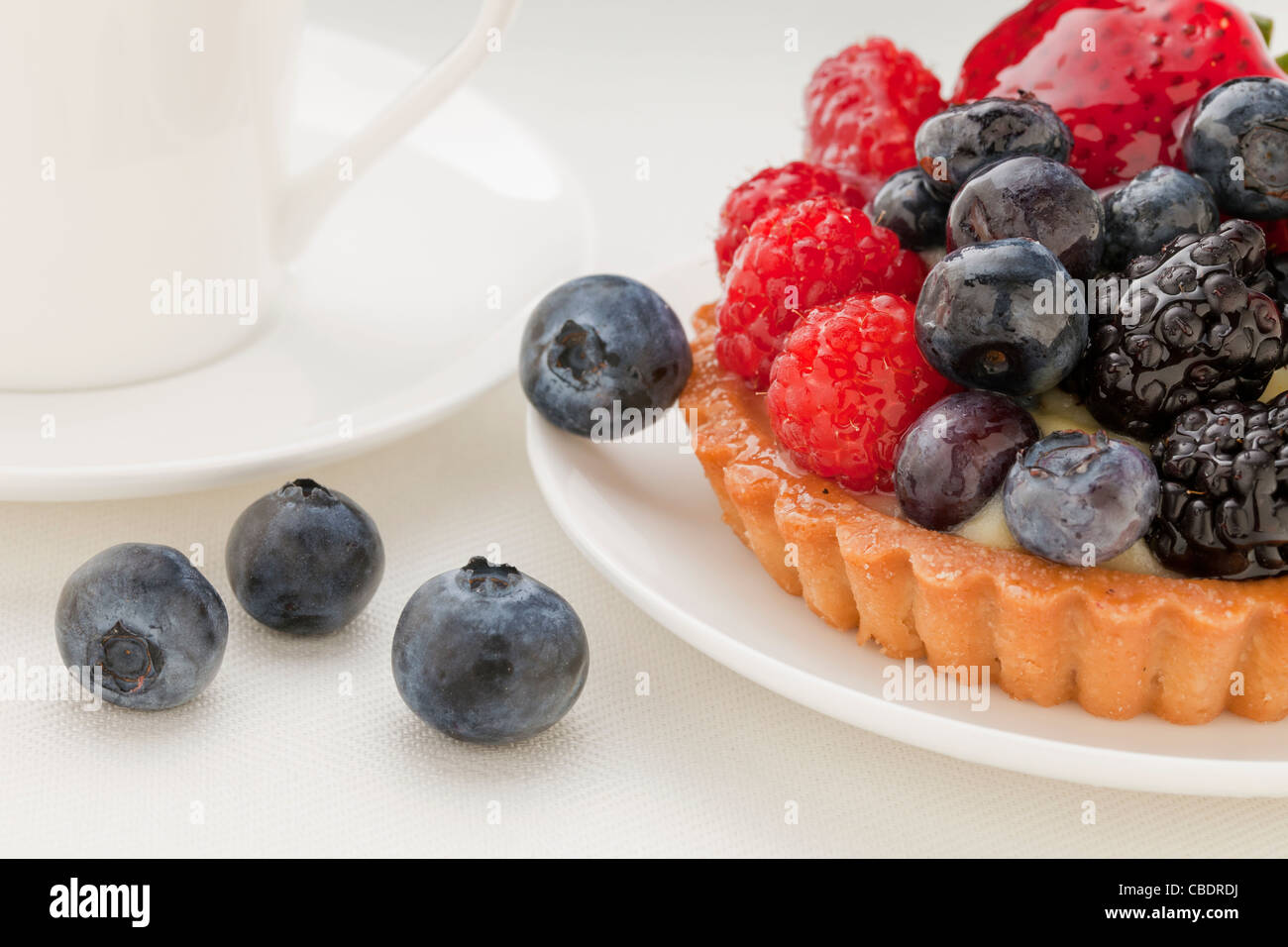 fruit tart with blueberry, blackberry, raspberry and strawberry, a coffee cup in background Stock Photo