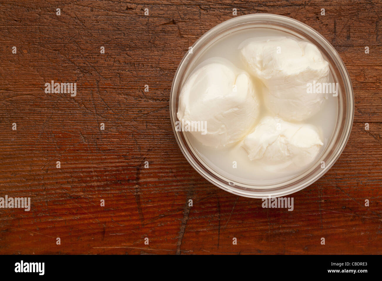 three balls of fresh mozzarella cheese in a glass bowl on scratched grunge wood surface Stock Photo