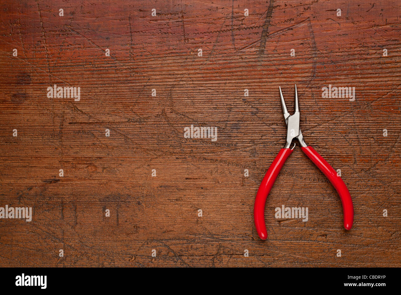 small needle nose pliers on a scratched and weathered wood background Stock Photo