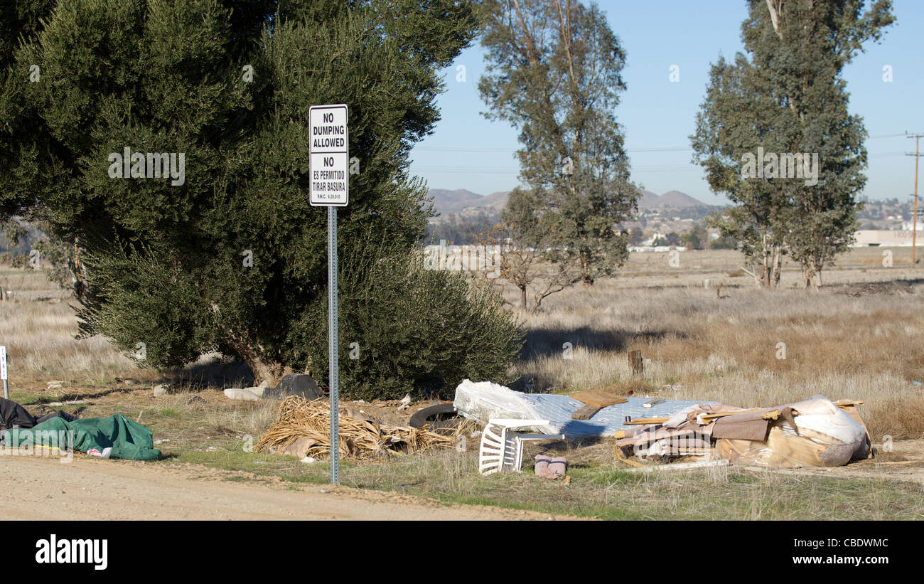 Trash alongside a dirt road next to a no dumping sign Stock Photo