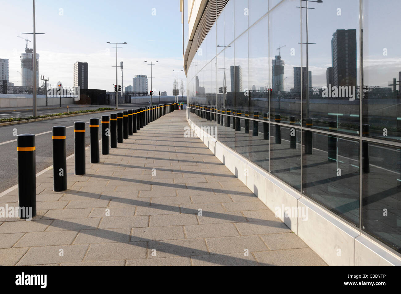 Long line of security bollards protection of pavement & buildings outside Stratford City Westfield shopping centre reflected in glass East London UK Stock Photo