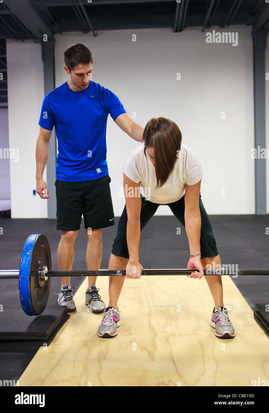 Male personal trainer coaching woman at lifting barbell weights. Stock Photo