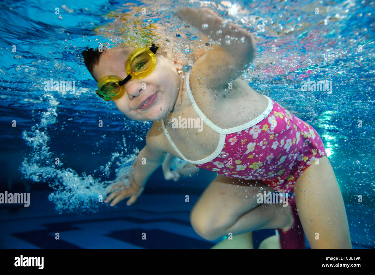 happy smiling two years old toddler girl swimming underwater holding