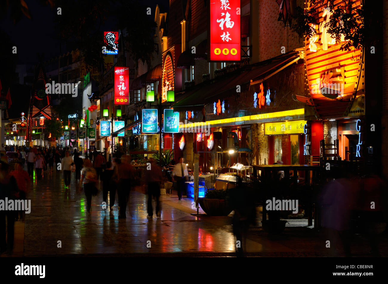 Pedestrians on Zeng Yang Bu Xing Jie street in Guilin on a rainy wet night with lights of shops and restaurants Peoples Republic of China Stock Photo