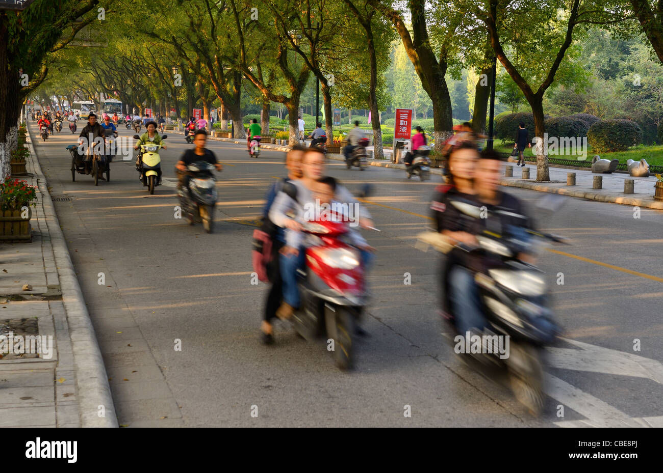 Morning rush hour in Guilin China with motorcycles on tree lined Bin Jiang Lu road Stock Photo