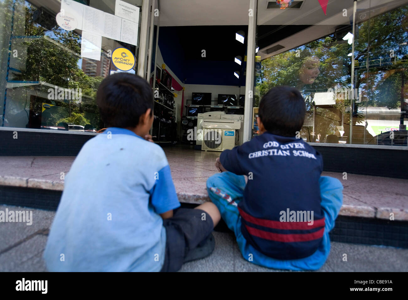 Children watching television trough the glass window of a shop from the street of Asuncion Paraguay Stock Photo