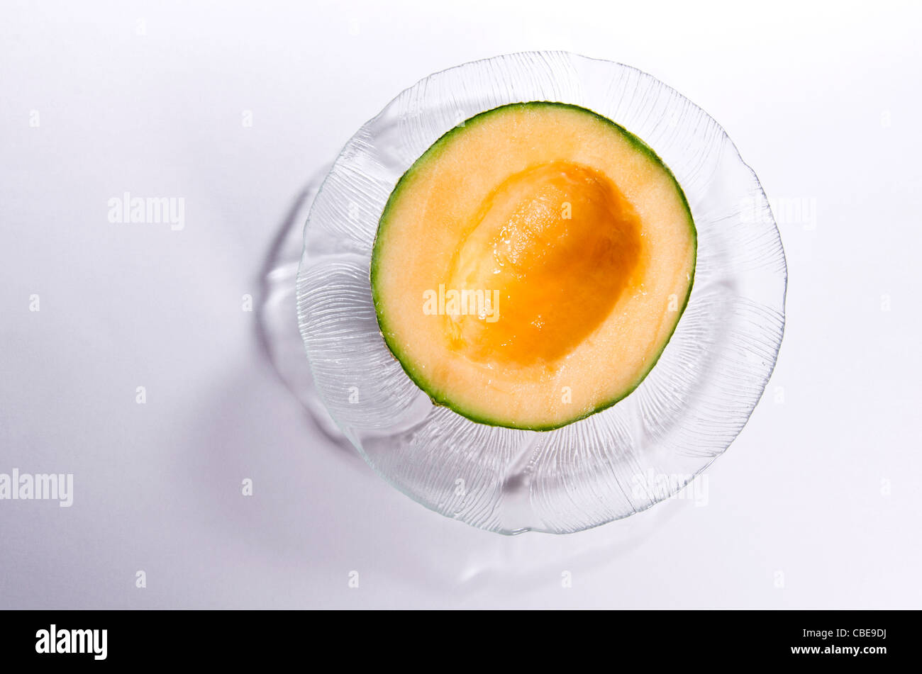 Half a cantaloupe, cut open, seeds scooped out, sitting on a glass plate. Stock Photo