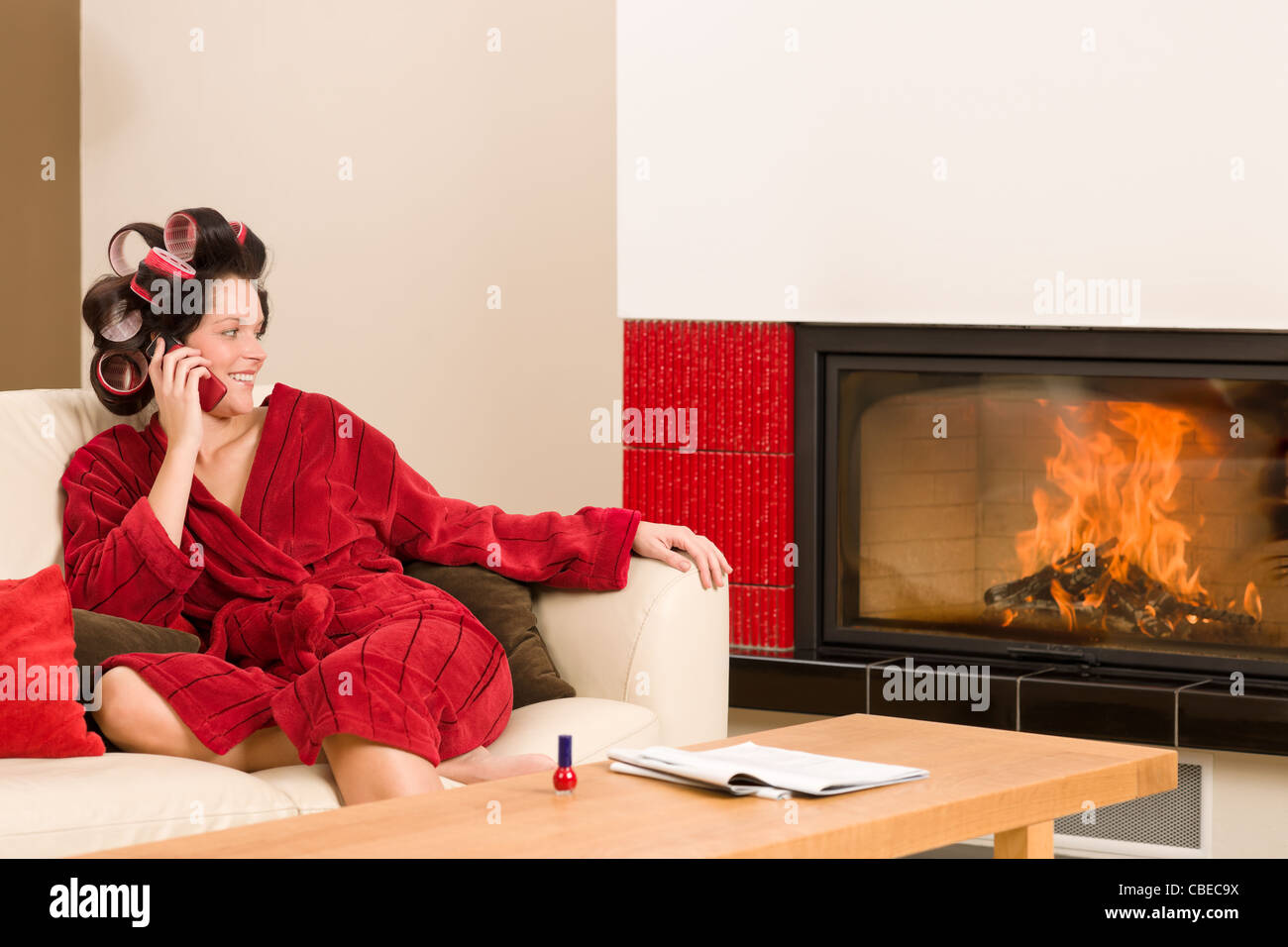 Home beauty woman with curlers calling phone fireplace red bathrobe Stock Photo