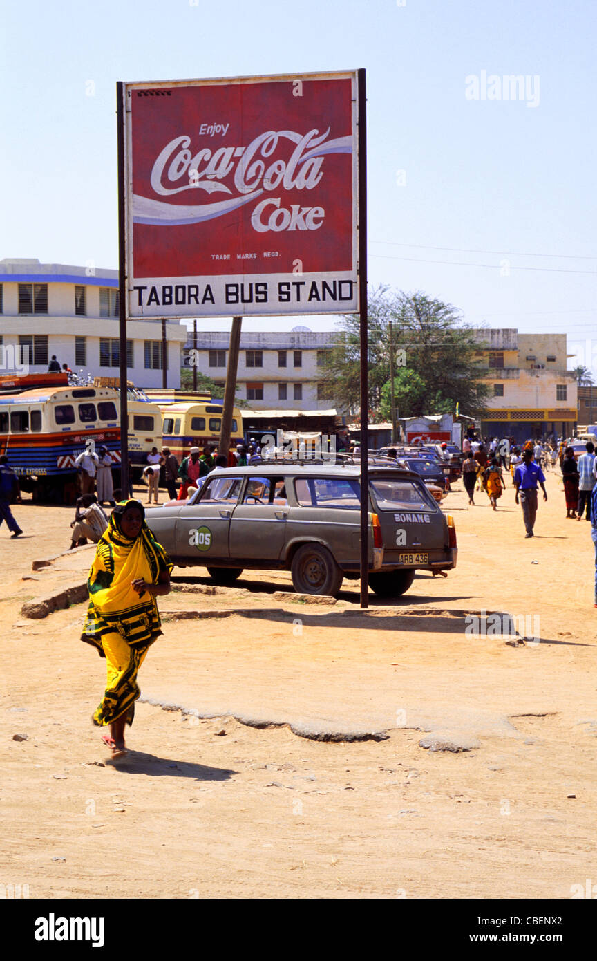Tabora, Tanzania. Town Bus Stand with Coca Cola sign and Peugeot 505 taxi with woman in yellow wrap. Stock Photo
