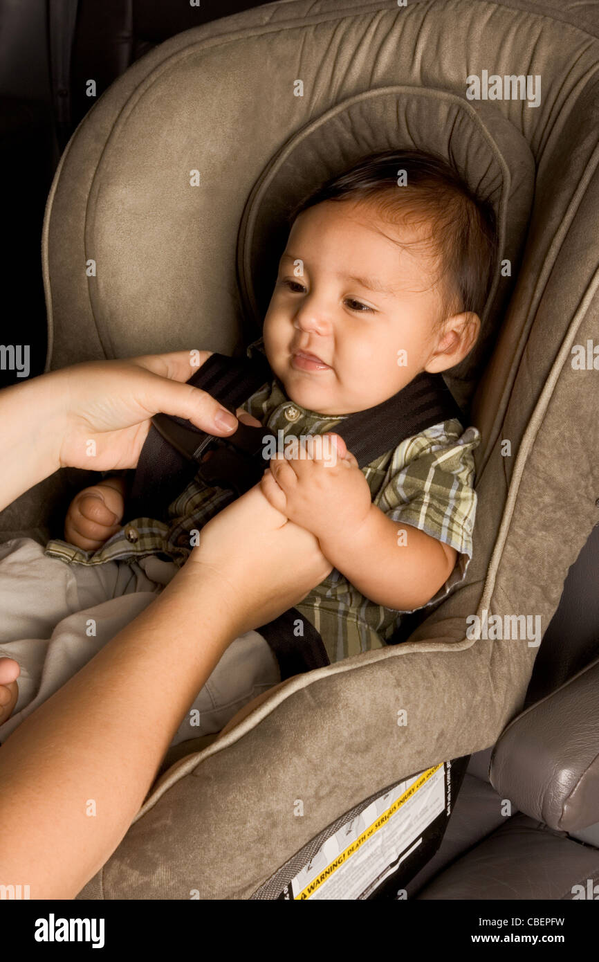 Smiling biracial Asian Filipino kid sitting in car seat while parent hands buckle him up Stock Photo