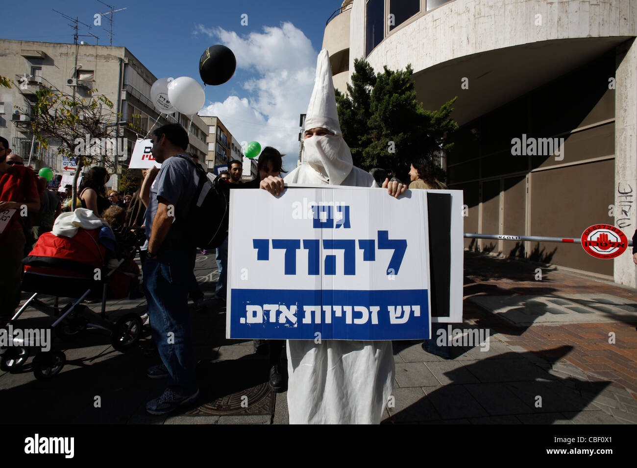 A right wing supporter dressed as Ku Klux Klan KKK member holds a sign in Hebrew reading 'A Jewish person has also human rights' as thousands of people participated in a rally to mark the international Human Rights Day in Tel Aviv Israel Stock Photo