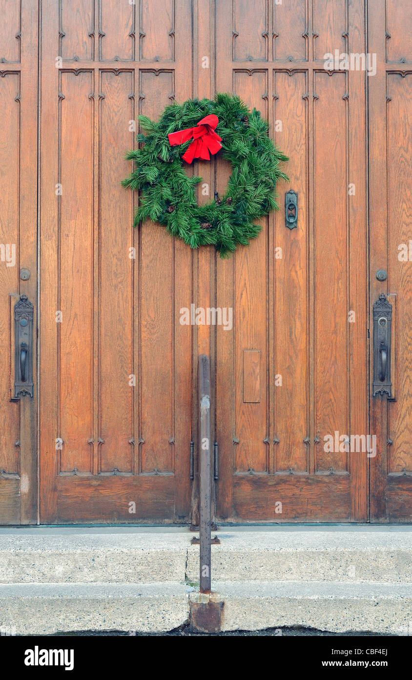Evergreen wreath with a red ribbon on a church door.  Wreaths are common decoration during the Christmas season. Stock Photo