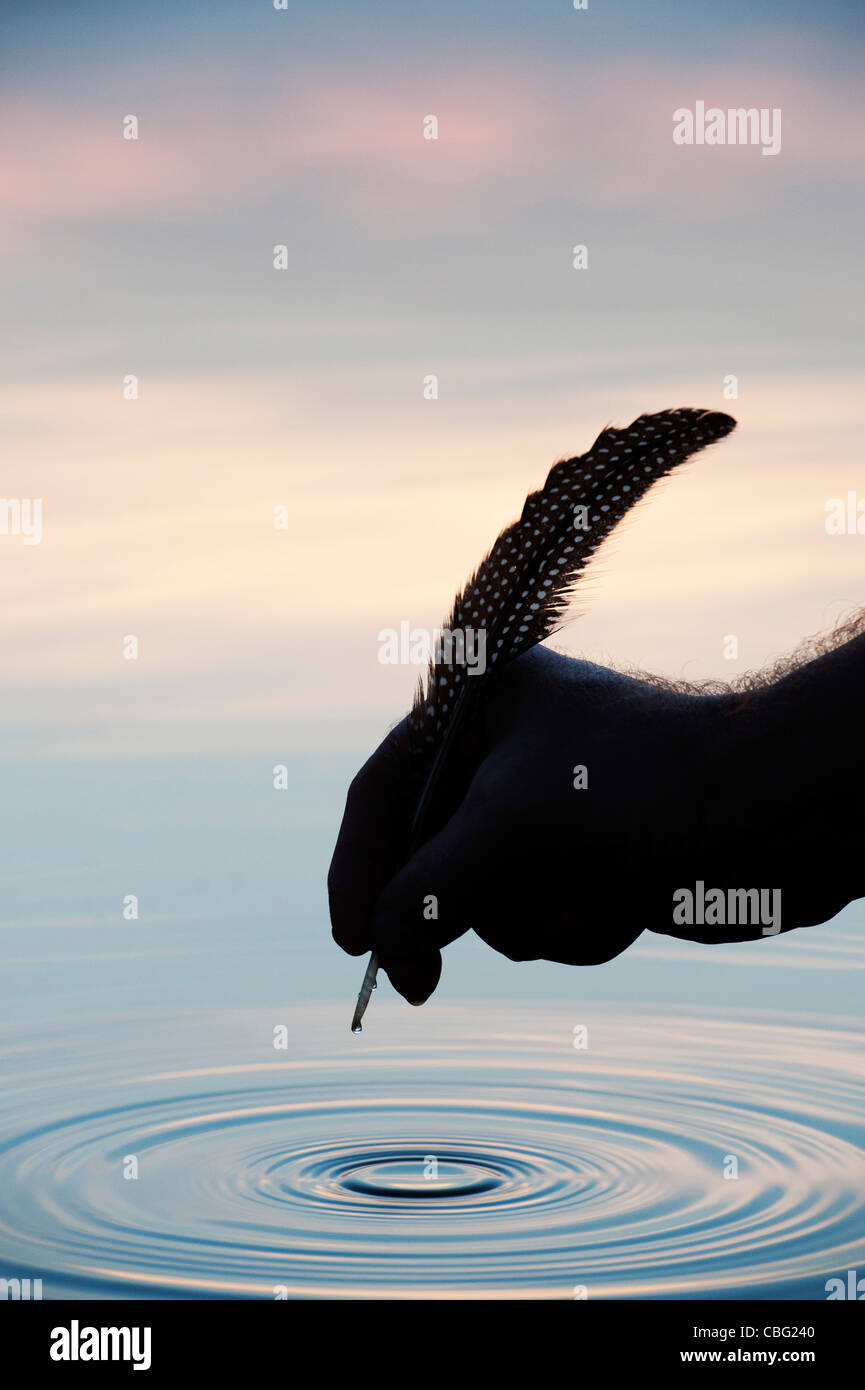 Hand holding quill over water with ripple silhouette Stock Photo