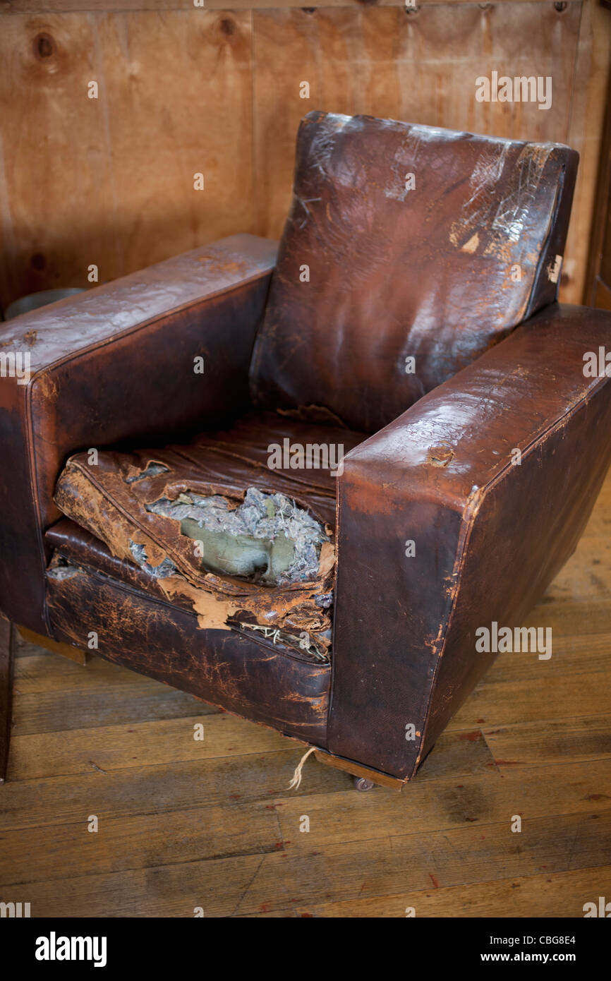 An old weathered leather armchair with torn cushion Stock Photo