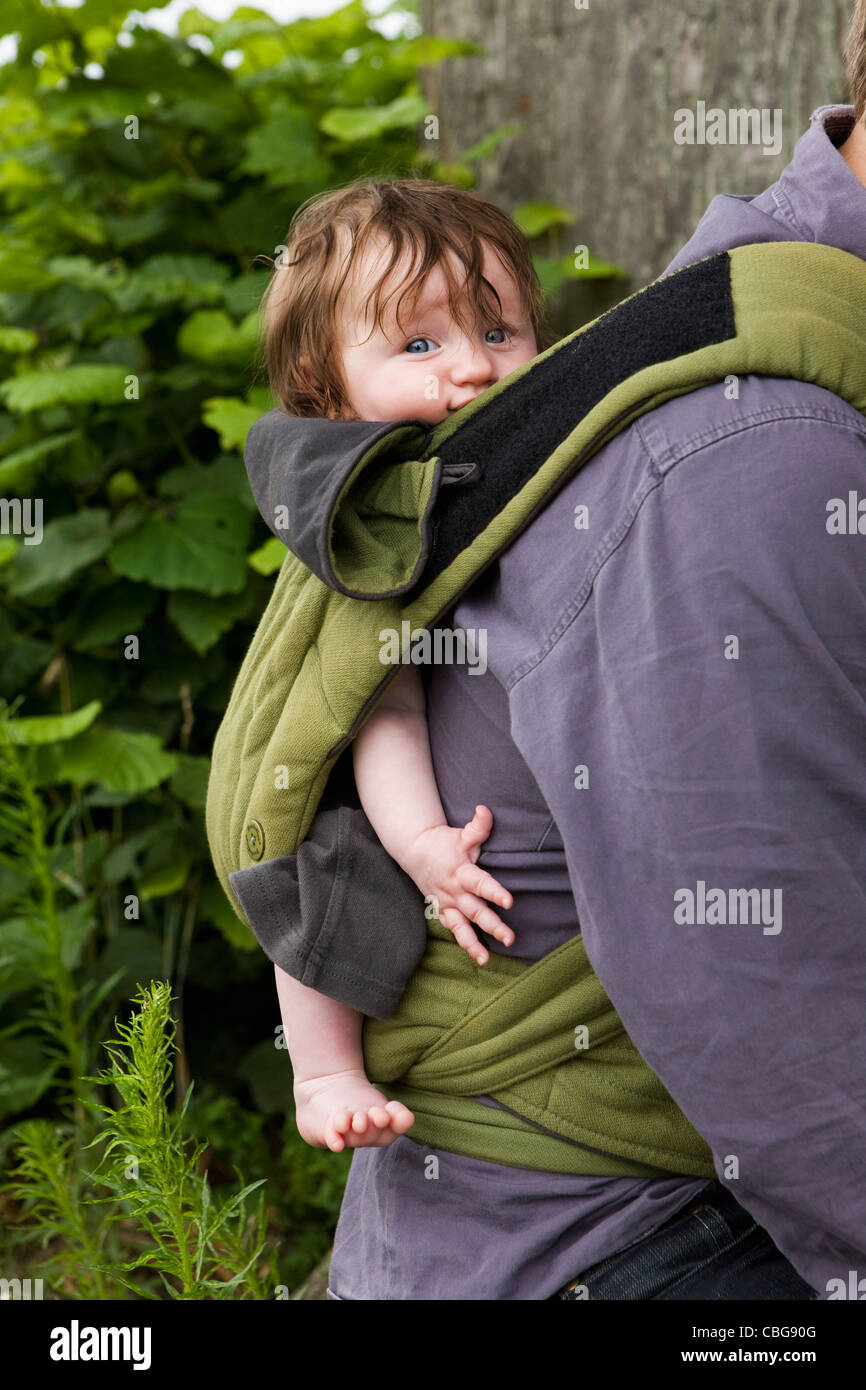 A father carrying his baby daughter in baby carrier, focus on baby Stock Photo