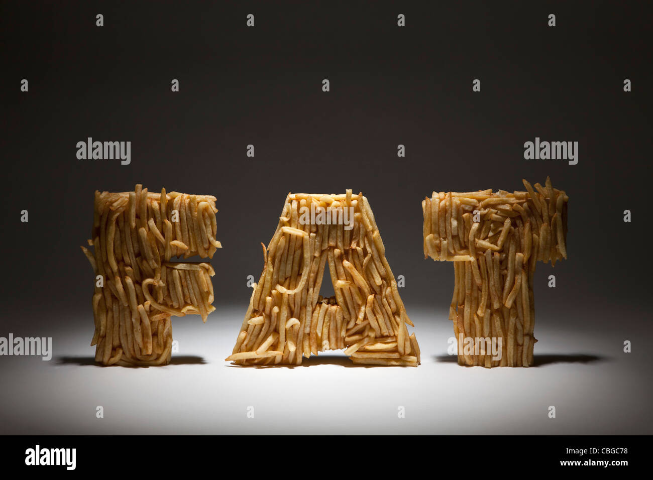 French fries molded to make the word FAT, spot lit Stock Photo