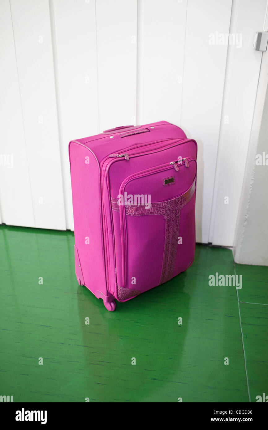 Pink suitcase contrasted against green floor and white door Stock Photo