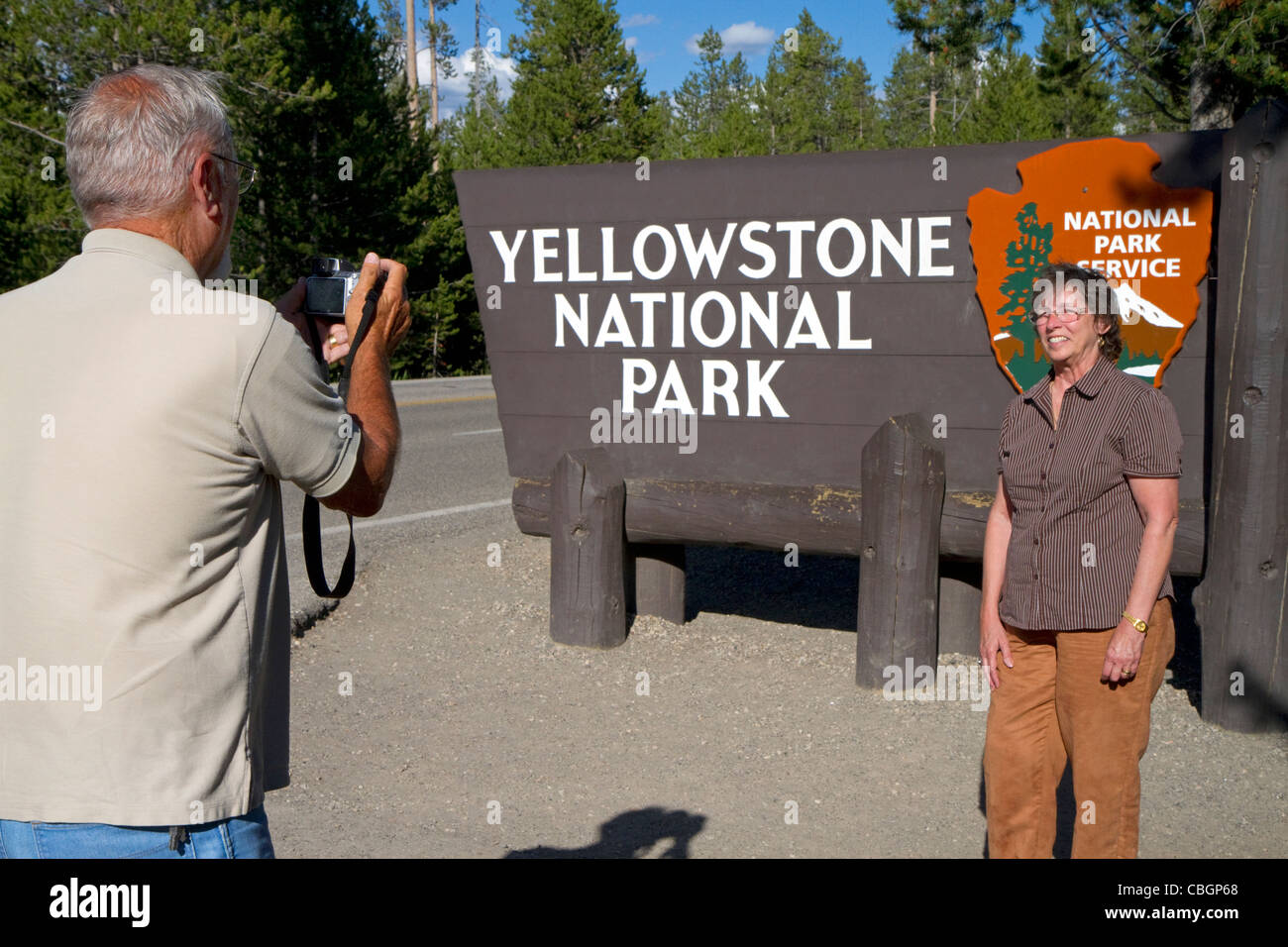 Tourists take a photo in front of the Yellowstone National Park entrance sign, West Yellowstone, Montana, USA. Stock Photo