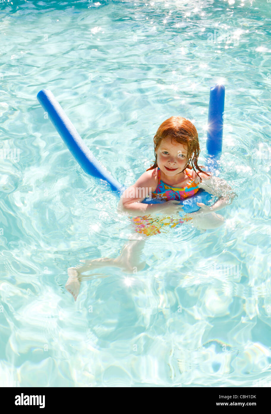 Red haired, young girl, aged 5, swimming in a swimming pool on a summer holiday. Using a float to aid swimming. Stock Photo