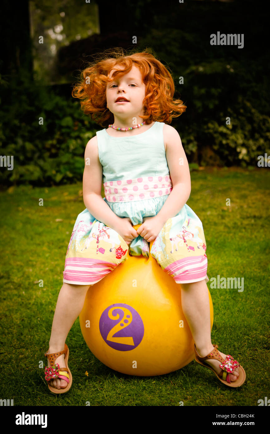 Little girl, aged 5, bouncing on a space hopper, in a summer garden. Stock Photo