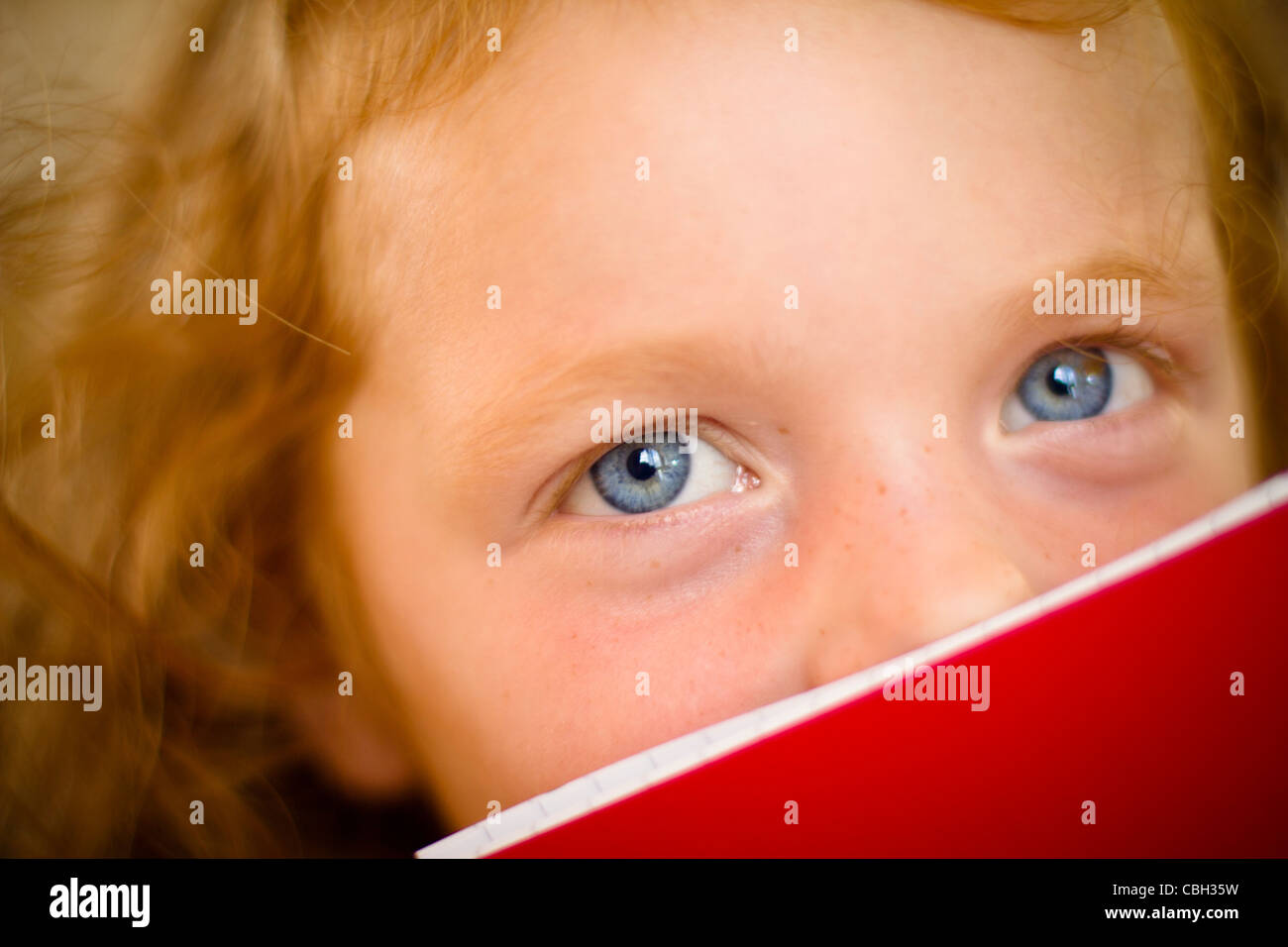 Little girl, aged 5, peering over the top of her book. Stock Photo
