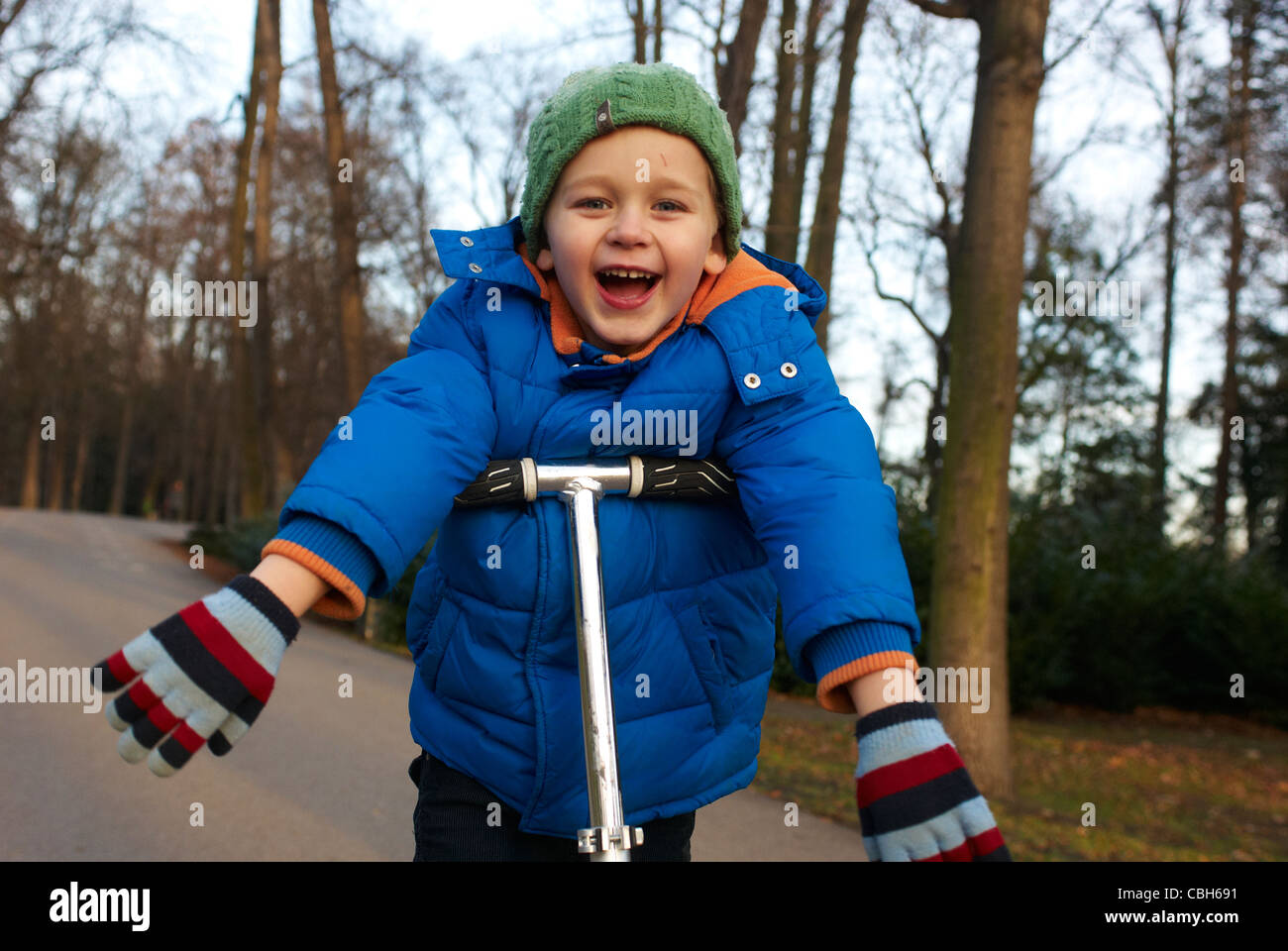 A young child blond boy on a scooter in park without safety helmet Stock Photo Alamy