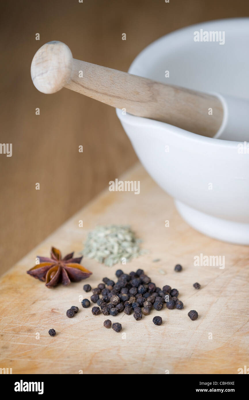 a porcelain pestle and mortar with black peppercorns, star anise and fennel seeds on a wooden chopping board Stock Photo