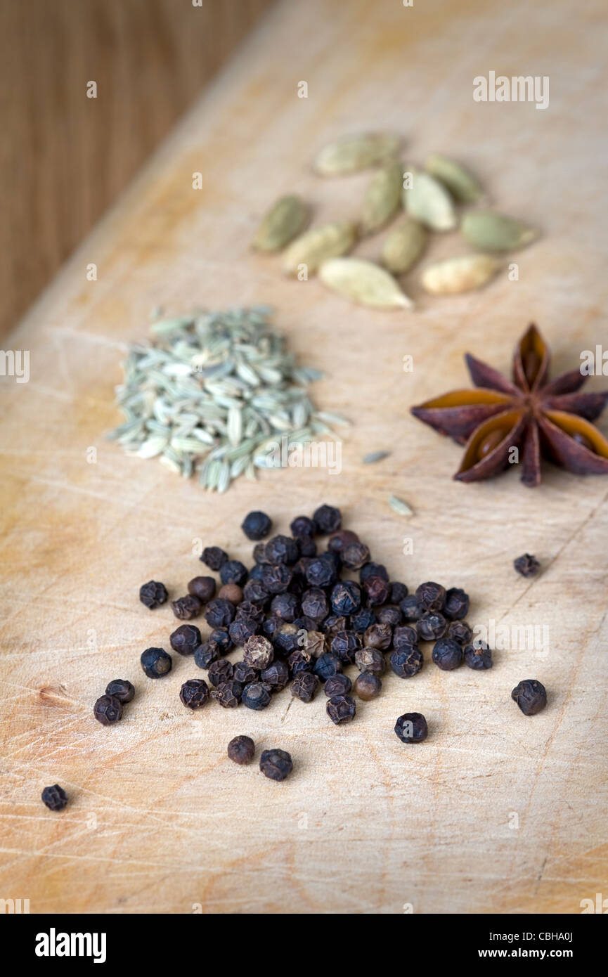 black peppercorns, star anise, fennel seeds and cardamom pods on a wooden chopping board Stock Photo