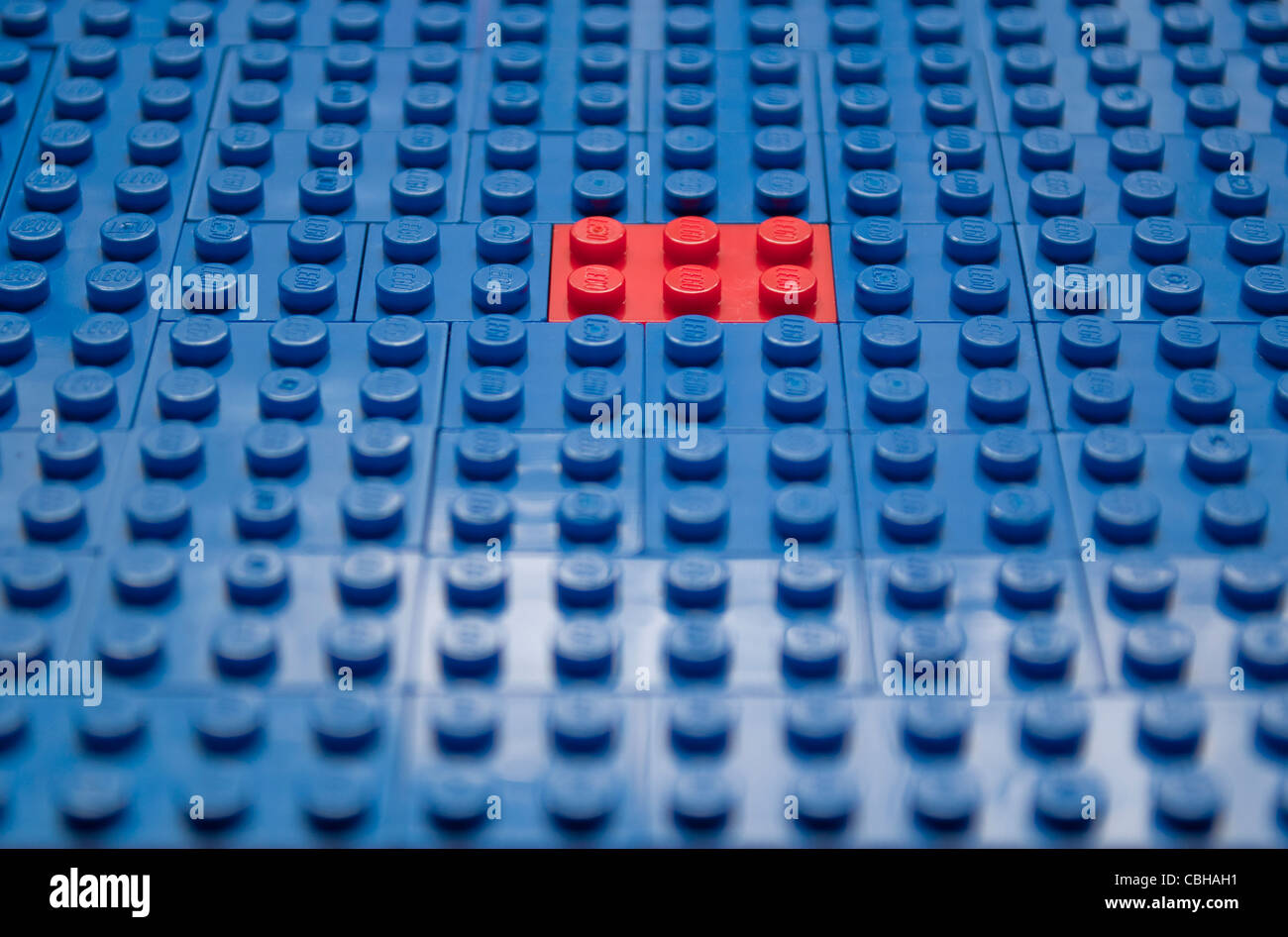 Bright red toy brick alone among bright blue bricks Stock Photo