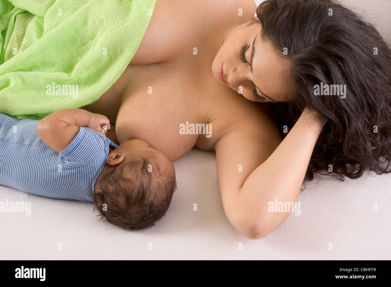 Latina woman lying on bed and breastfeeding her 2 months old baby of mixed Hispanic and African-American ethnicity Stock Photo