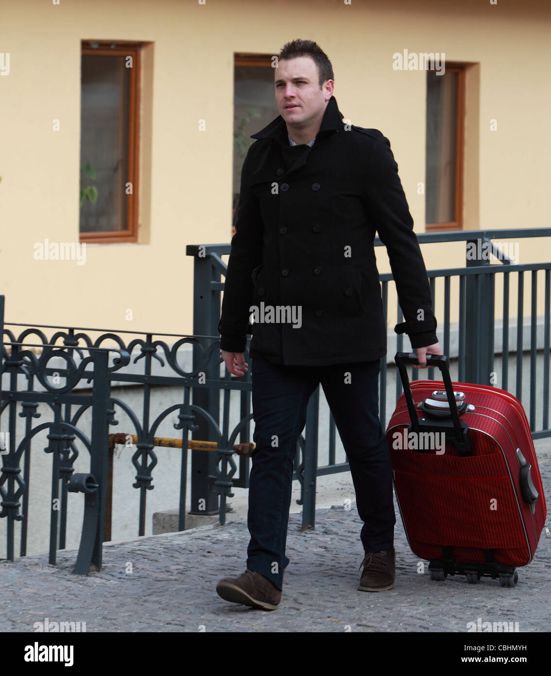 Young man with a red suitcase in a small cobbled street in a city. Stock Photo