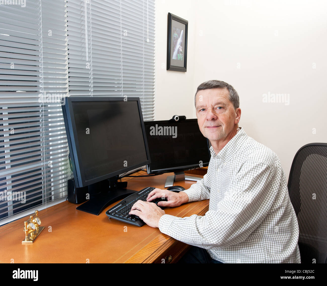 Senior executive in home office with two monitors and keyboard on