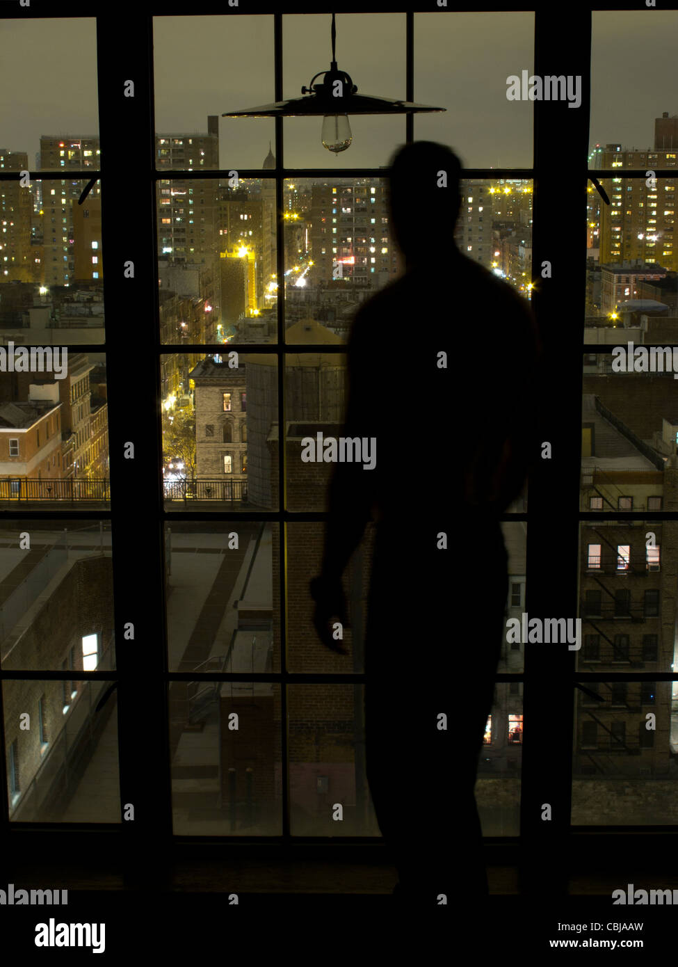 Silhouette of Man at window at night overlooking downtown Manhattan, New York City, New York, USA Stock Photo
