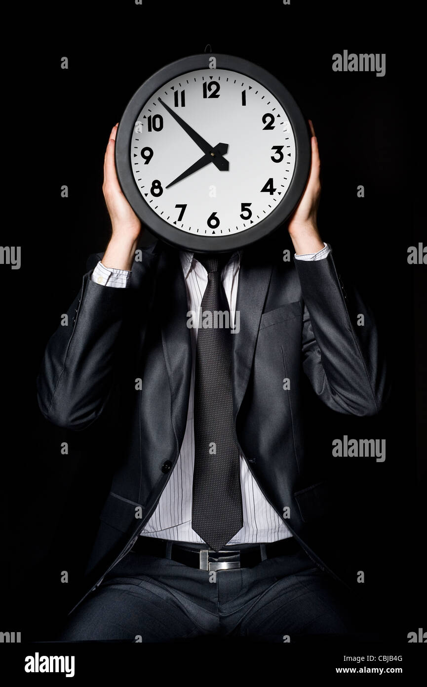 man in gray suit holding big clock covering his face Stock Photo