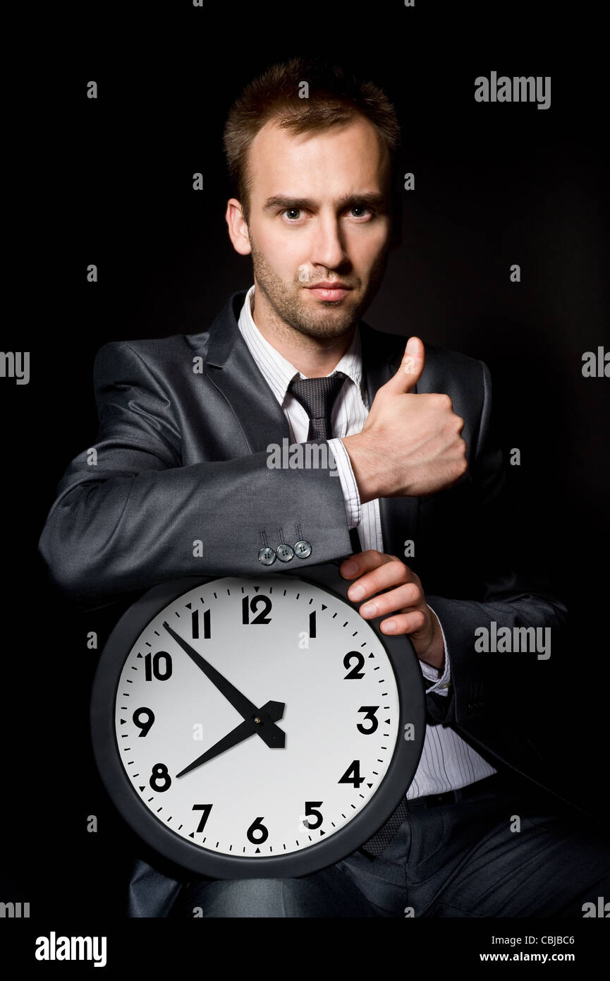 handsome business man holding clock, showing his thumb up Stock Photo