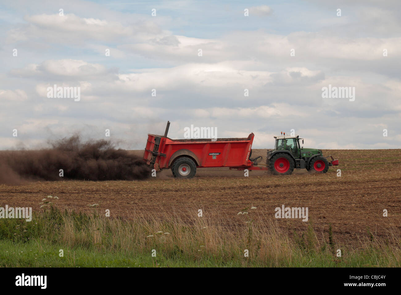 Tractor with Sodimac manure spreader (epandeur de fumier) spreading manure on an uncultivated field in northern France. Stock Photo