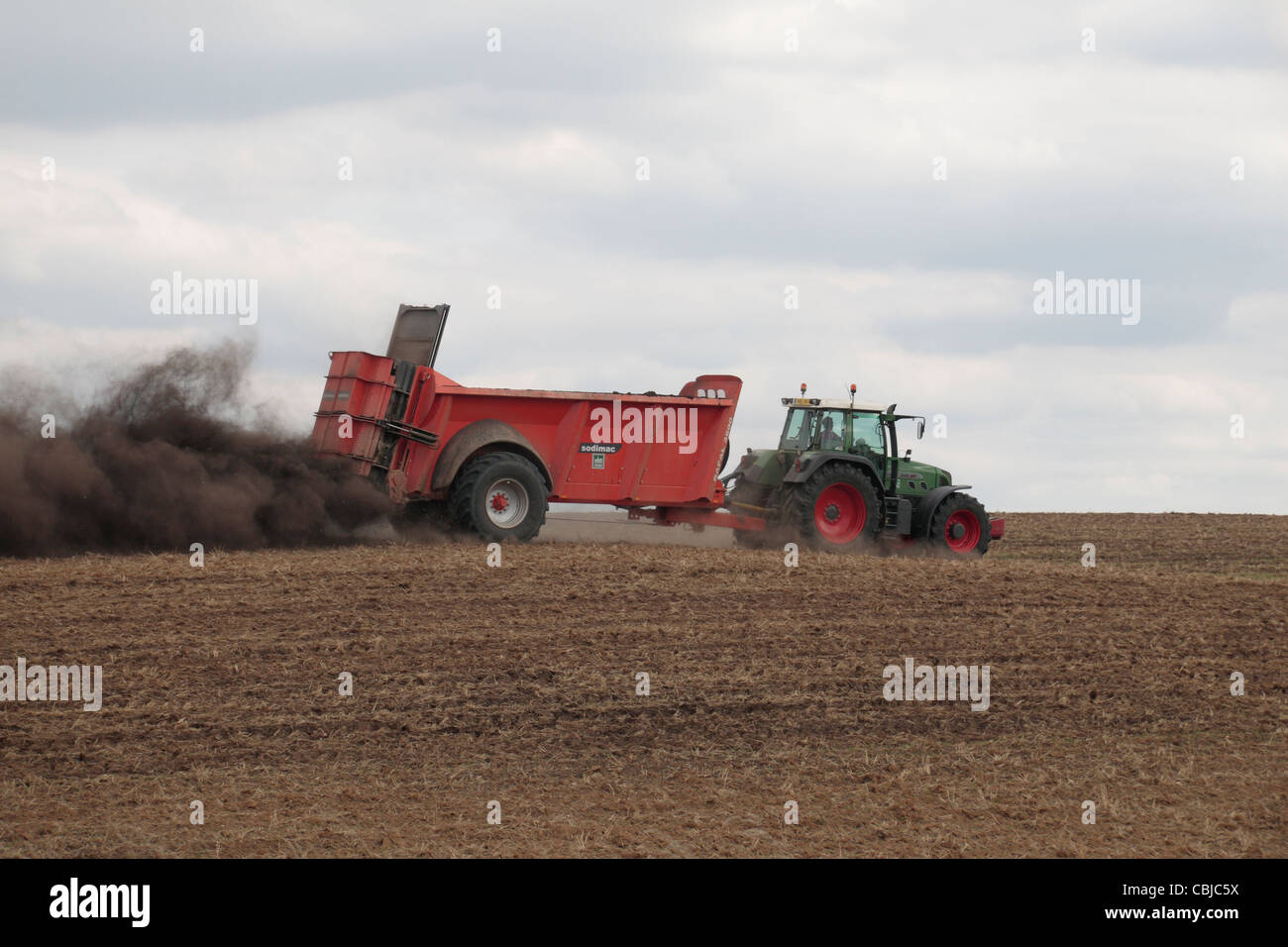 Tractor with Sodimac manure spreader (epandeur de fumier) spreading manure on an uncultivated field in northern France. Stock Photo